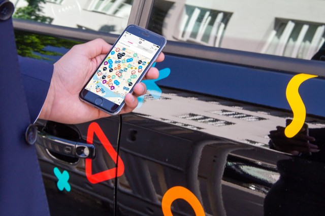 A person standing in front of a car using the Free2Move app, which enables to have access to different sharing providers using one account